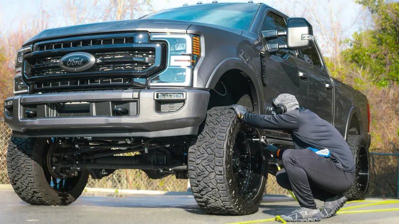 Detailer hand-drying the wheels of a lifted Ford F-250 Super Duty after an exterior detail