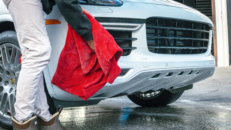 Detailer drying a white Porsche Cayenne with a plush towel after an exterior detail
