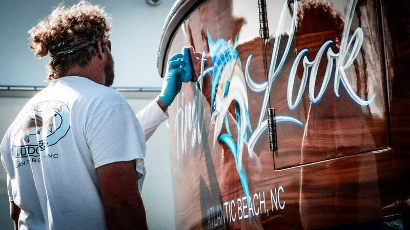 Detailer hand-applying ceramic coating to the glossy mahogany-look transom of a sportfishing boat