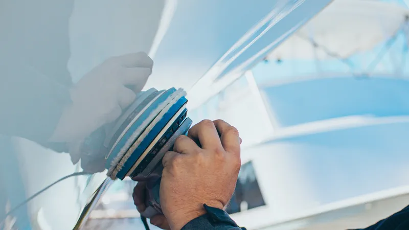 Detailer machine-polishing the white hull of a sportfishing boat dockside